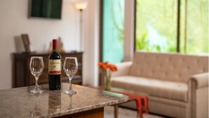 A wine bottle and two glasses on a table in a room with a large window, a sofa, and a TV on the wall. - Casita Escondida (Antigua Guatemala)