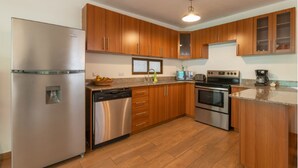A modern kitchen with stainless steel appliances, wooden cabinets, and a granite countertop. - Casita Escondida (Antigua Guatemala)