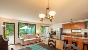 A modern kitchen with wooden cabinets, a dining area with a wooden table and chairs, and a large window overlooking a garden. - Casita Escondida (Antigua Guatemala)