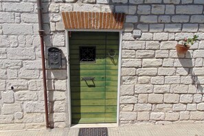 A white brick building with a green door, a small window with a decorative grille, and a number '64' sign on the wall.