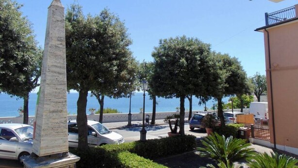 Une vue sur la mer avec un grand monument, des voitures garées et des arbres.