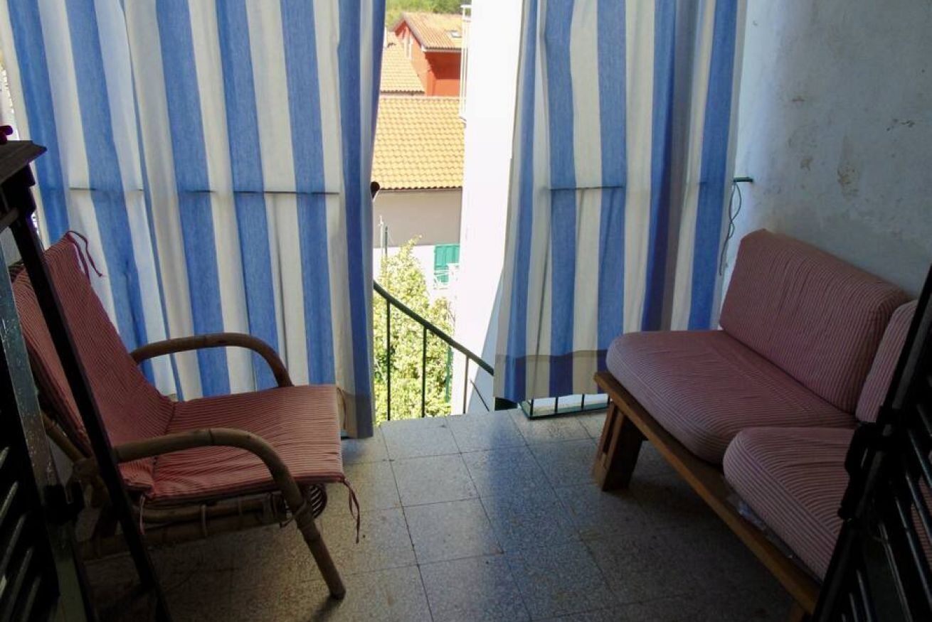 A balcony with striped curtains, a red cushioned chair, and a wooden sofa.