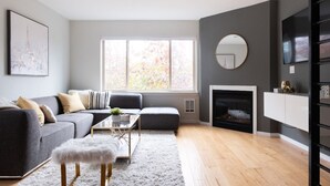 A modern living room with a grey sofa, a white ottoman, a coffee table, and a fireplace. - Modern Central District Townhouse — 1 Block from Judkins Park Light Rail, Patio (Seattle)