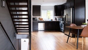 A modern kitchen with dark cabinets, a stainless steel refrigerator, and a wooden dining table. - Modern Central District Townhouse — 1 Block from Judkins Park Light Rail, Patio (Seattle)
