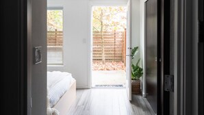 A room with a bed, a door leading to an outdoor area with a wooden fence and a tree, and a potted plant. - Modern Central District Townhouse — 1 Block from Judkins Park Light Rail, Patio (Seattle)