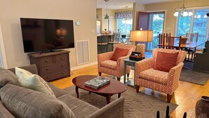 Un salon comprenant un canapé, des fauteuils, une table basse, un téléviseur et un coin repas avec une table et des chaises.
