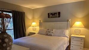 Une chambre à coucher bien rangée, avec un lit, deux tables de chevet, une commode, un vase décoratif et une fenêtre avec des rideaux.