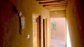 Un couloir étroit avec un plafond et des murs en bois rustique, une porte donnant sur l’extérieur et une petite plante placée dans l’embrasure de la porte.