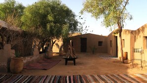 Une cour extérieure agrémentée d’un bâtiment de style traditionnel, d’un foyer et de diverses plantes et arbres.