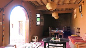 Une pièce chaleureuse avec une table ronde, un canapé et une table à manger avec des chaises. Il y a une fenêtre avec vue, une porte donnant sur l’extérieur et un plafond orné de lampes en osier.