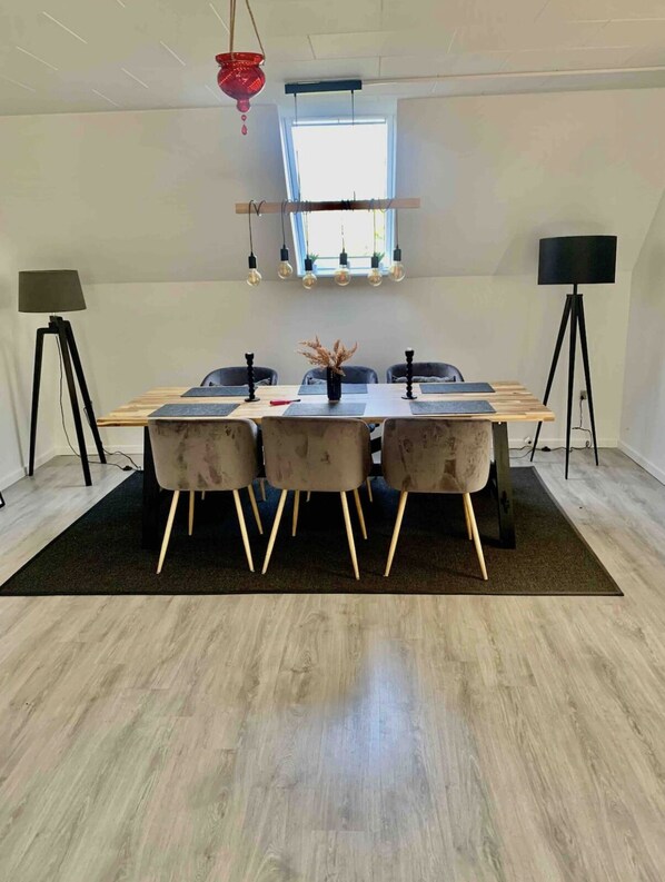 Een moderne eetruimte met een houten tafel, drie stoelen met zachte kussens, een vaas met gedroogde bloemen en hanglampen.