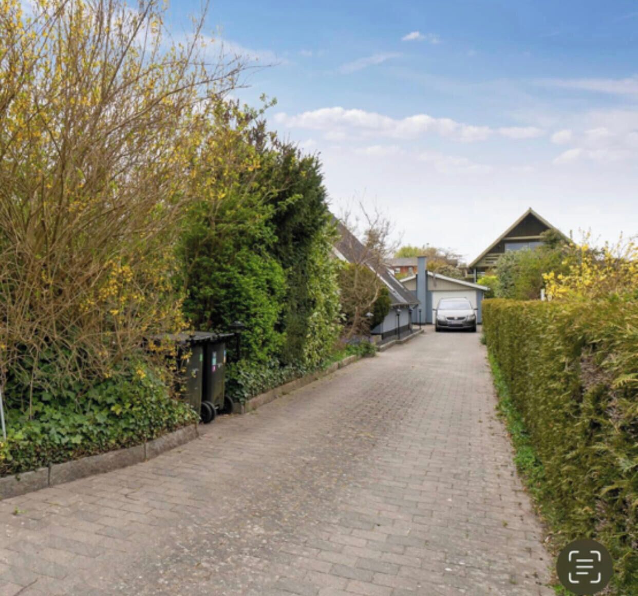 A paved road flanked by greenery and a building in the distance.