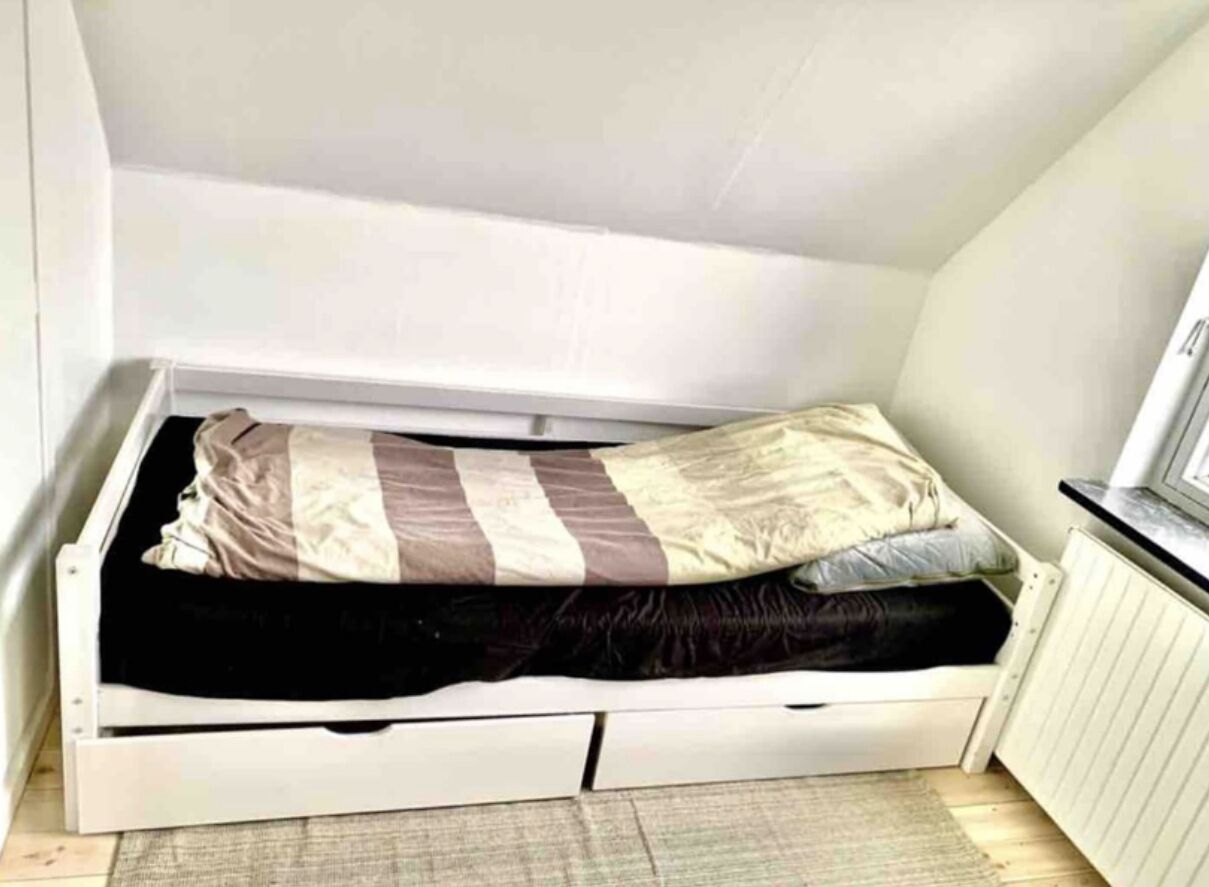 Een kleine, witte eenpersoonskamer met een eenvoudig design, een klein raam en een radiator aan de muur.