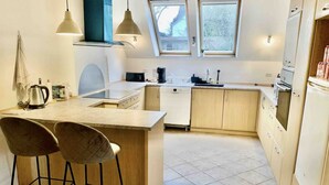 A compact kitchen with a central island, two bar stools, a coffee machine, and a dishwasher.