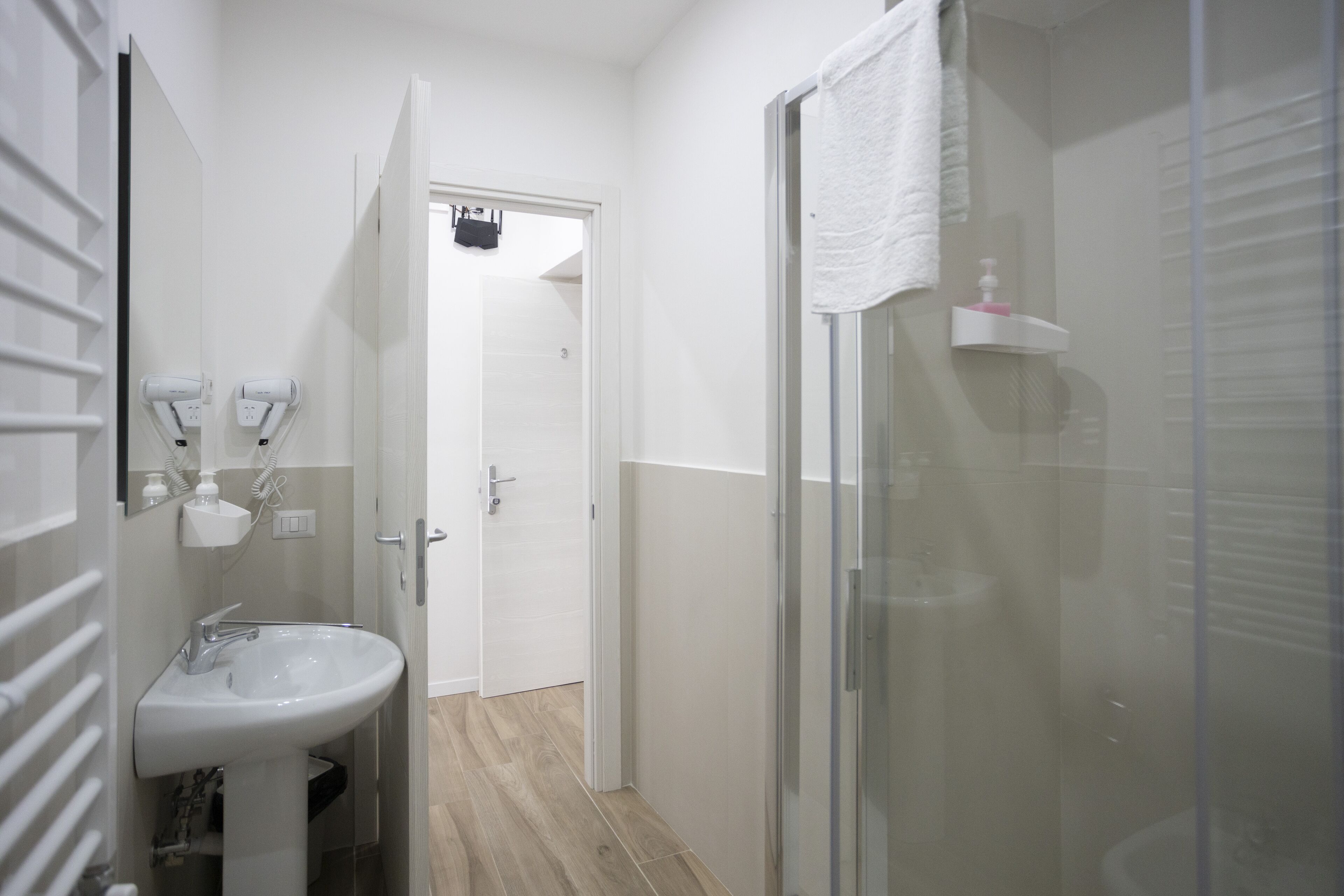 Un baño con un lavamanos blanco, cabina de ducha con paredes de vidrio y una puerta que da a otra habitación.