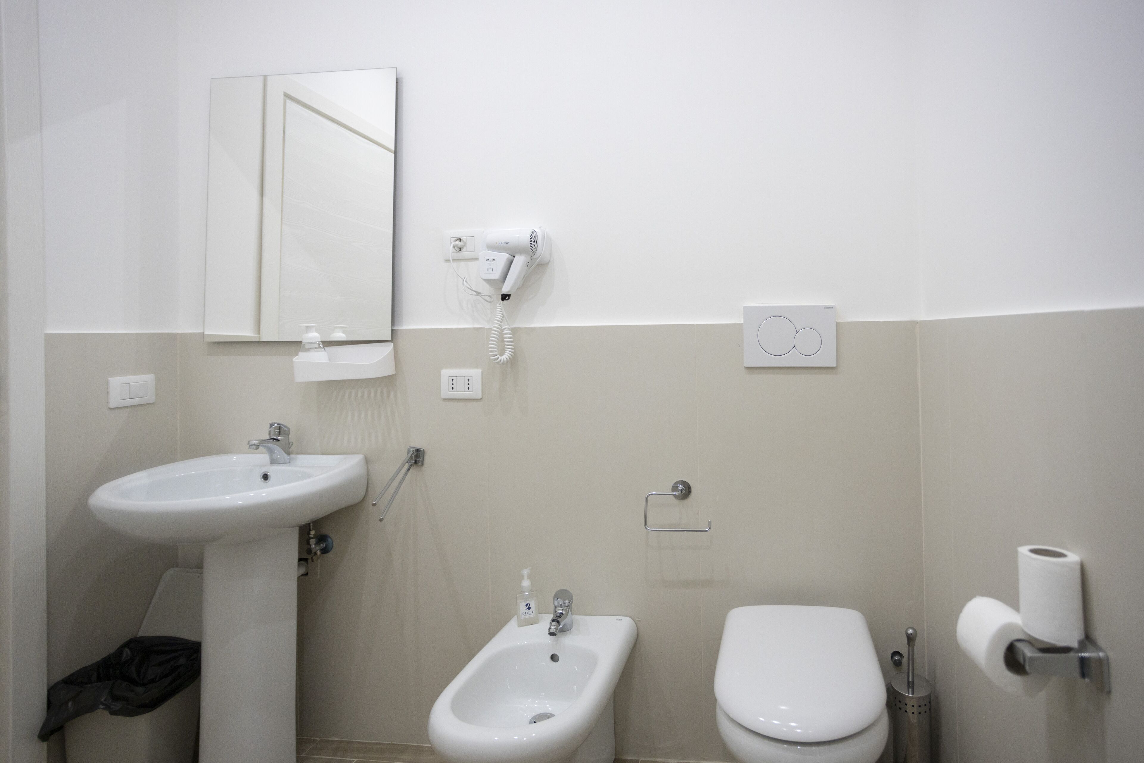 A bathroom with a sink, bidet, toilet, and a hairdryer mounted on the wall.