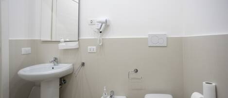 A bathroom with a sink, bidet, toilet, and a hairdryer mounted on the wall.