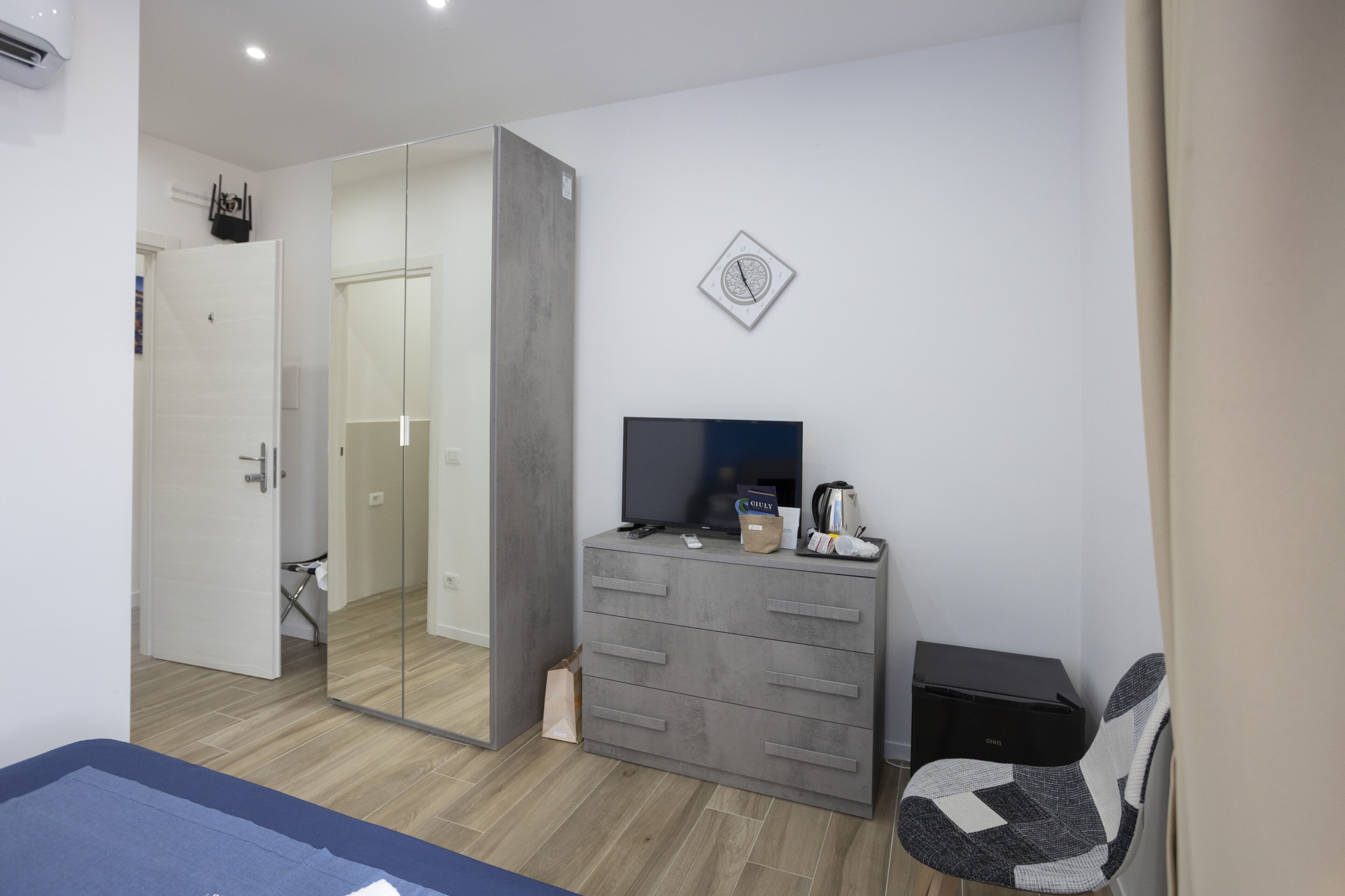 A modern bedroom with a large mirror, a TV, a coffee maker, and a desk.