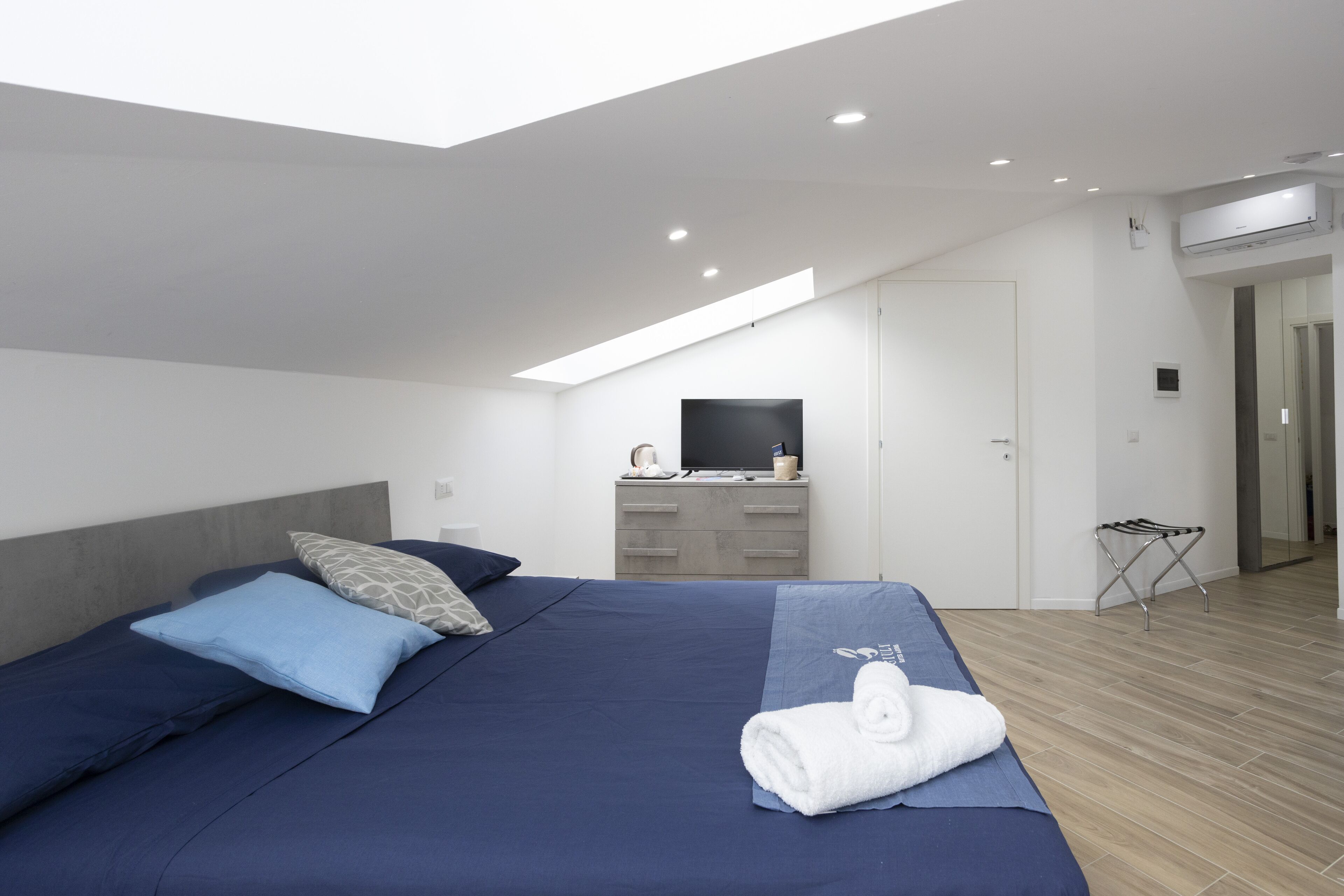 A modern bedroom with a large bed, a flat-screen TV, a desk, and a walk-in closet.