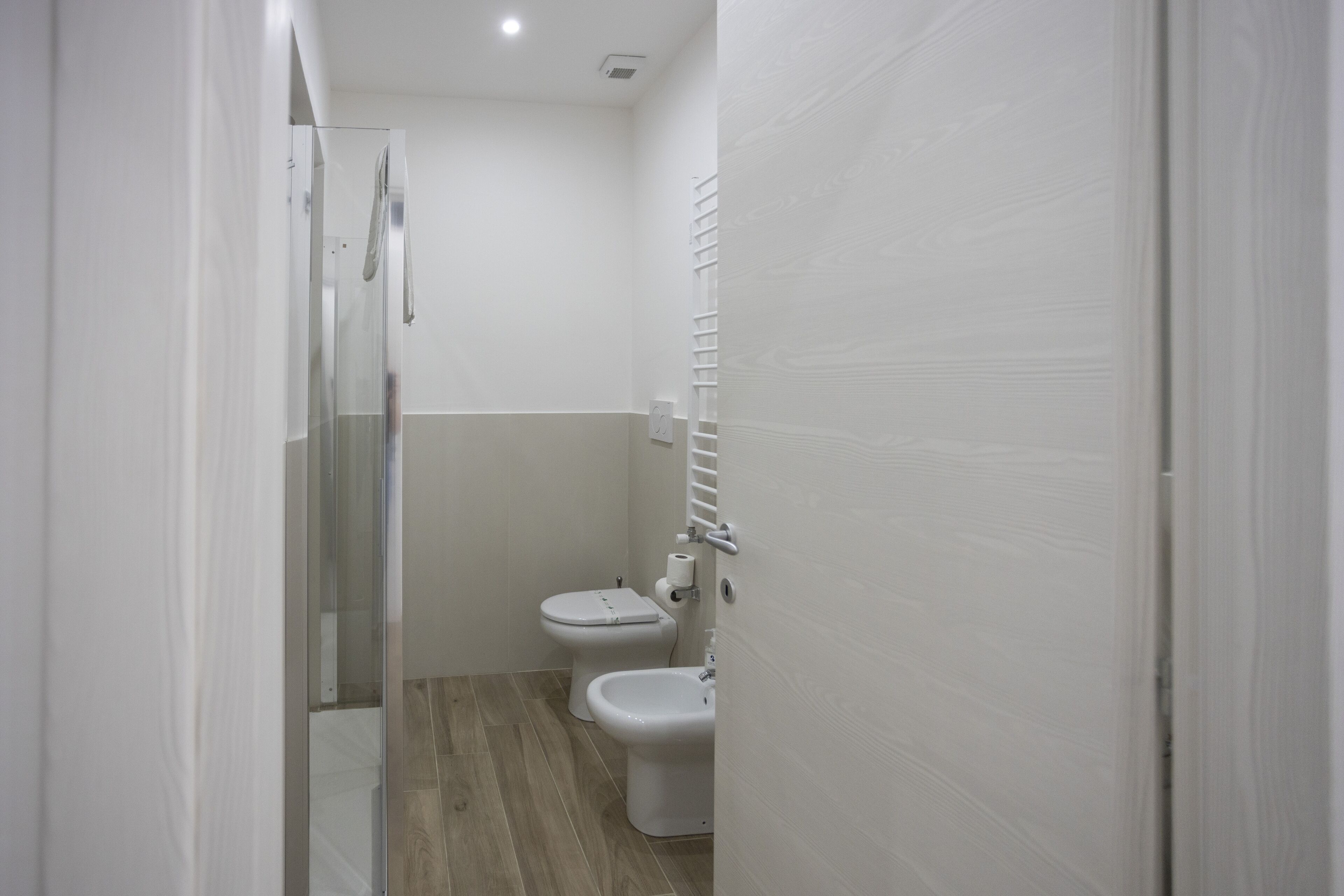 A narrow bathroom with a shower, toilet, and bidet.
