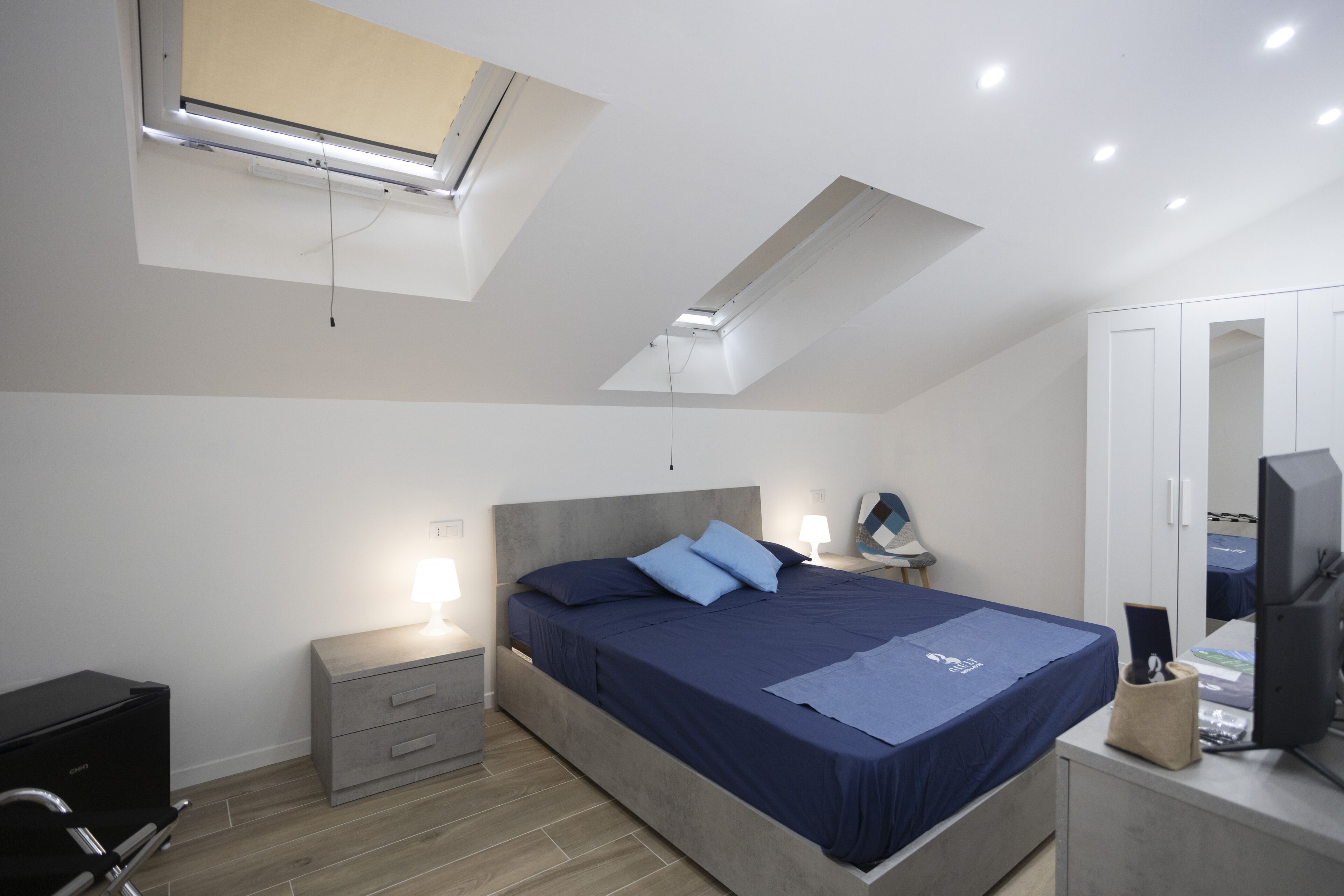 A bedroom with a bed, bedside tables, a desk, a chair, a wardrobe, and a ceiling light.