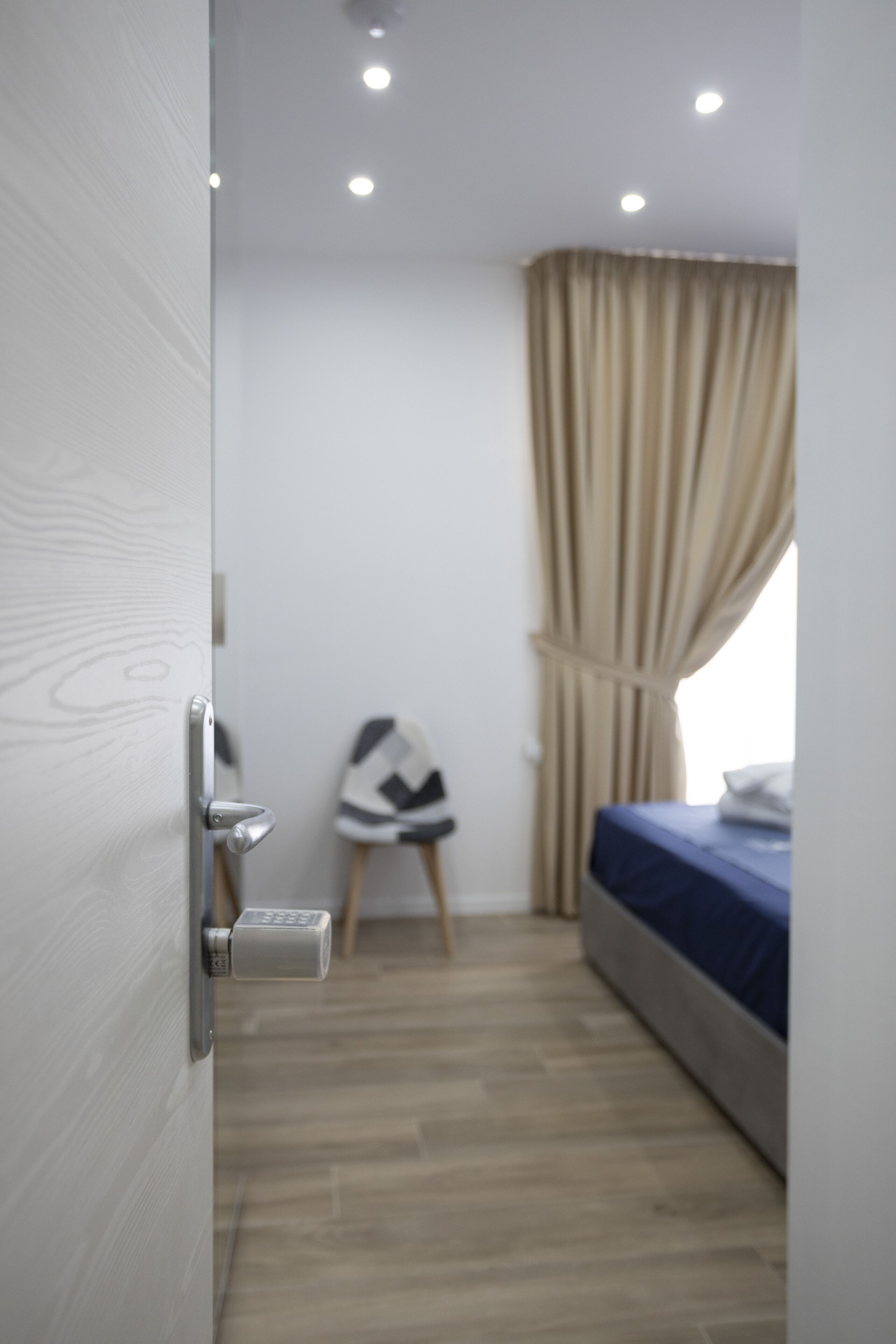Een moderne slaapkamer met een houten vloer, een bed met een blauwe deken, een stoel en een gordijn.