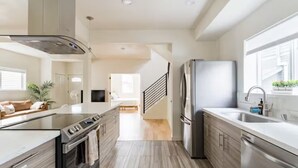 A modern kitchen with a central island, stainless steel appliances, and a view to the living area. - Central District 5BR — Walk to Capitol Hill, Cal Anderson Park & Broadway (Seattle)