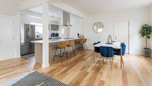 A modern kitchen with a central island, bar stools, and a dining area with a table and chairs. - Central District 5BR — Walk to Capitol Hill, Cal Anderson Park & Broadway (Seattle)