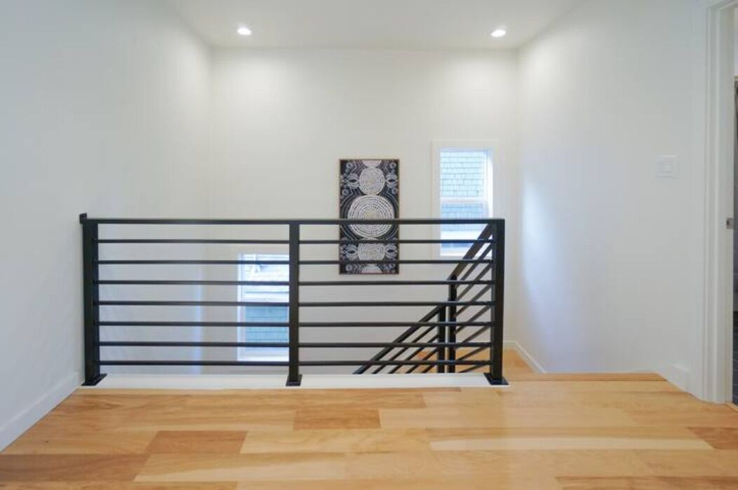A staircase with a black metal railing, a wooden floor, and a wall-mounted artwork.