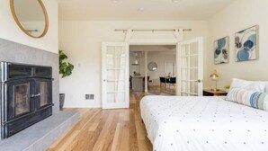 A bedroom with a fireplace, a bed with a white duvet, a wooden floor, and a door leading to a bathroom. - Central District 5BR — Walk to Capitol Hill, Cal Anderson Park & Broadway (Seattle)
