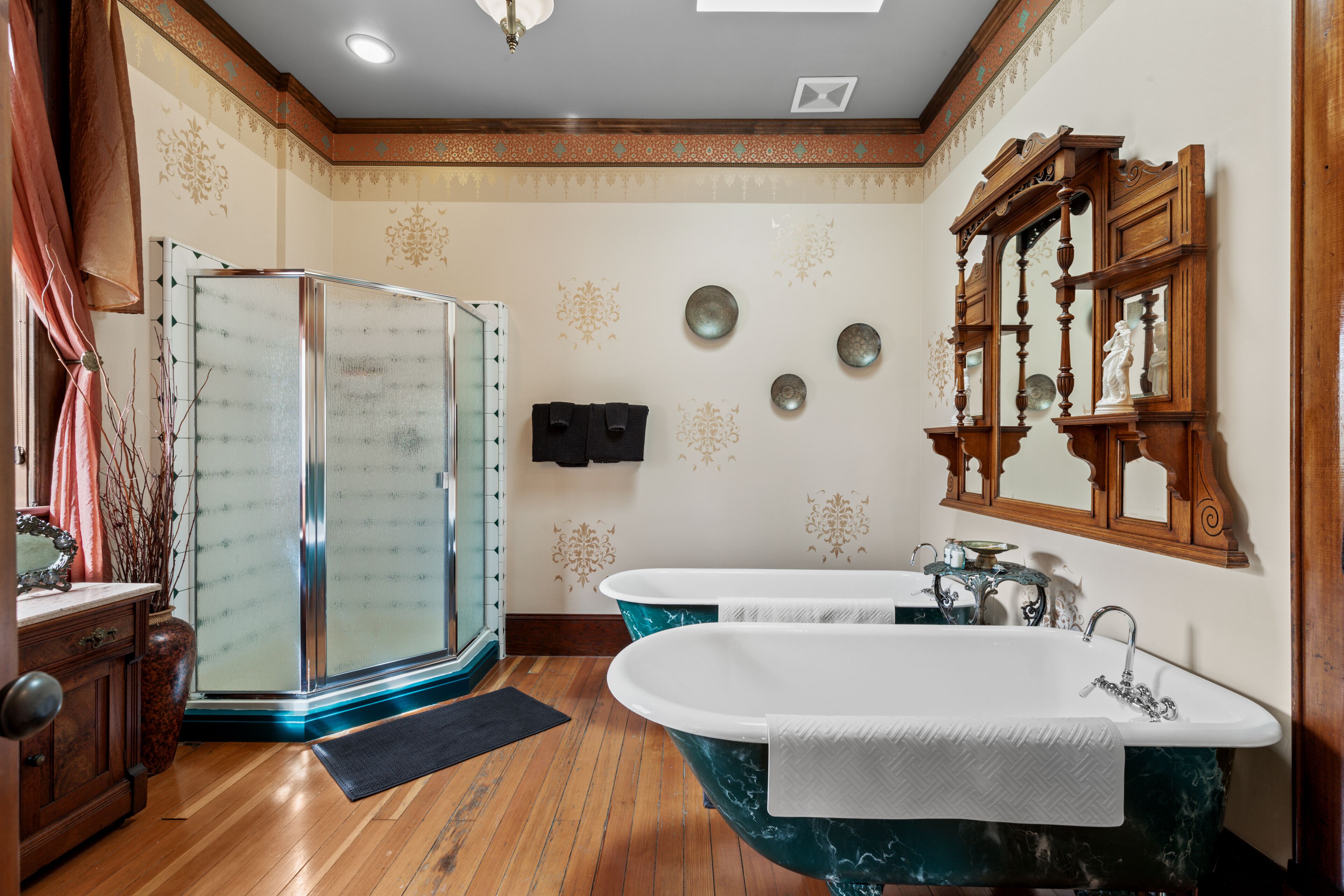 Un baño con dos tinas independientes, cabina de ducha de vidrio y tocador de madera con espejo.