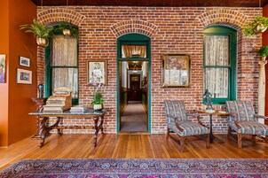 A room with a brick wall, wooden floor, green-framed windows, and two upholstered chairs.