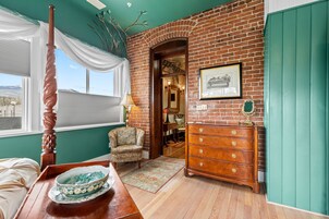 A room with a brick wall, a wooden dresser, a chair, and a bed.