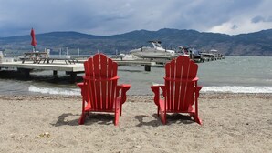 Dos sillas Adirondack rojas mirando un muelle con un bote, un embarcadero de madera y montañas al fondo.
