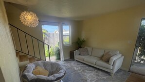 En stue med en sofa, en rund stol med hynder, en trappe og et stort vindue.