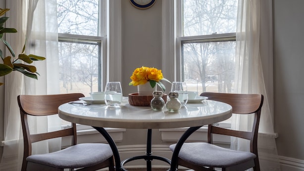 A round dining table with chairs, a clock on the wall, and a window with curtains.