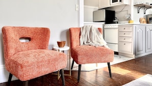 A modern kitchen with white cabinets, a microwave, and a stove. There are two orange chairs with a small table between them.