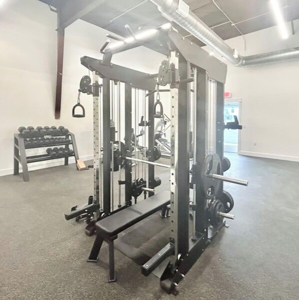A gym with a squat rack, bench press, and dumbbells.