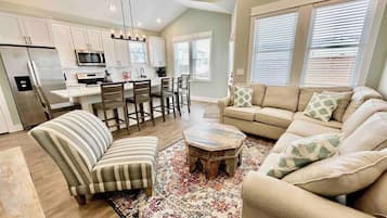 A modern living room with a sofa, armchair, coffee table, and a dining area with chairs and a table.