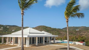 A modern building with a white roof and columns, surrounded by palm trees and a pool.