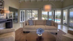 A spacious living room with a beige sofa, a coffee table, and a view of a swimming pool.
