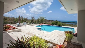 A modern outdoor pool area with a clear view of the ocean and hills in the background.