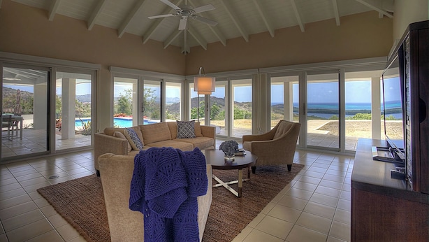 A spacious living area with a ceiling fan, large windows, a sofa, a coffee table, and a view of a pool and landscape.