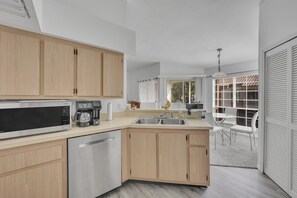 A modern kitchen with wooden cabinets, stainless steel appliances, and a large window offering a view of the outdoors.