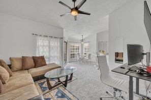 A modern living room with a sofa, a glass coffee table, a TV, and a computer desk.