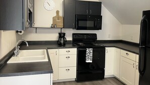Une cuisine avec un four noir, des placards blancs, un micro-ondes noir et une horloge au mur.