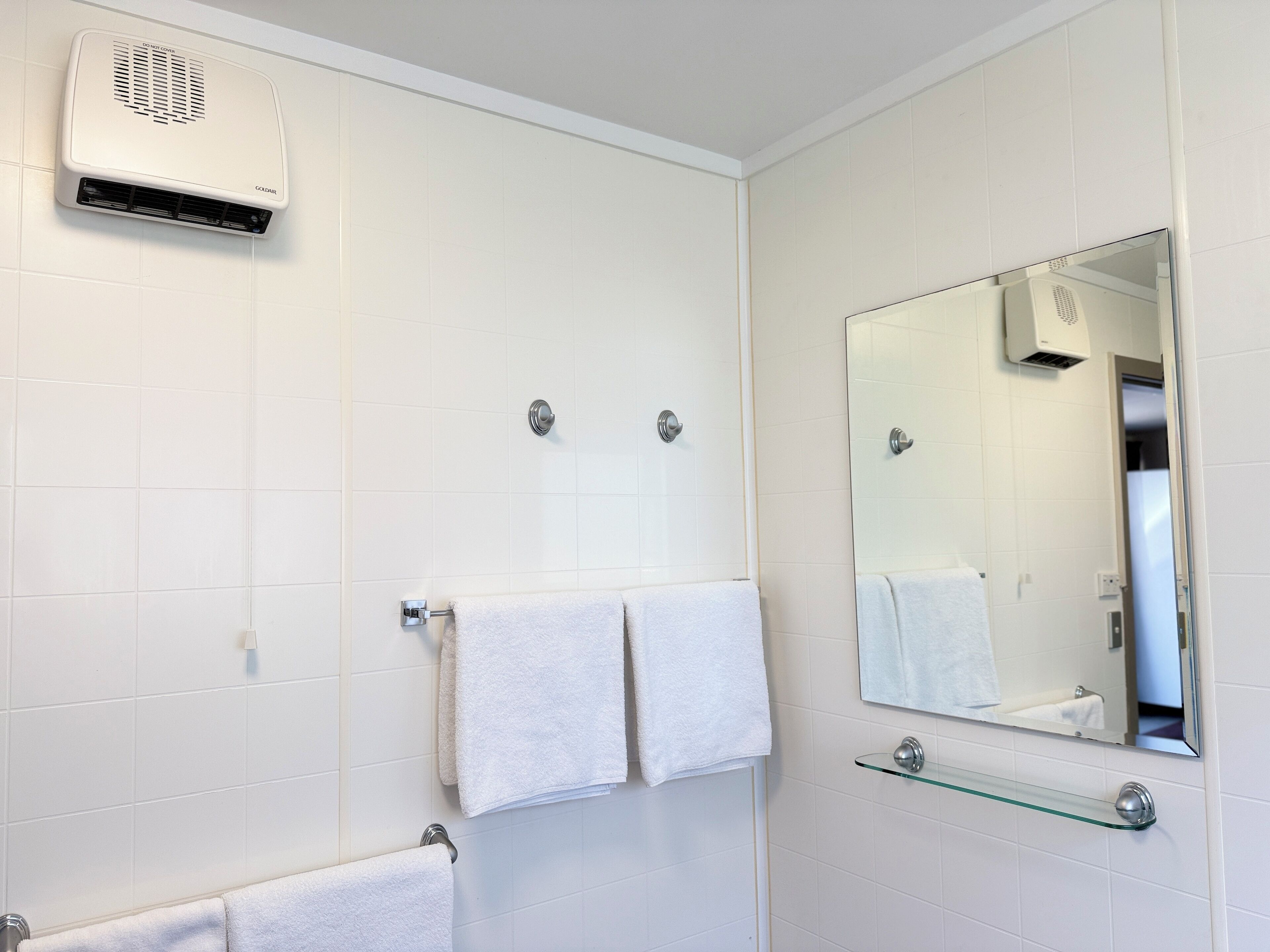 Une salle de bain moderne avec des carreaux blancs, une étagère en verre, un miroir et deux serviettes.