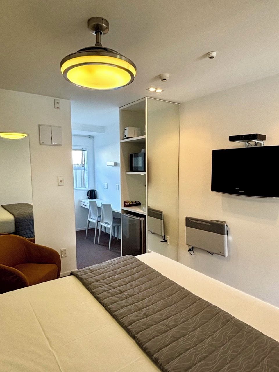 A hotel room with a bed, a desk, a chair, a television, and a ceiling light.