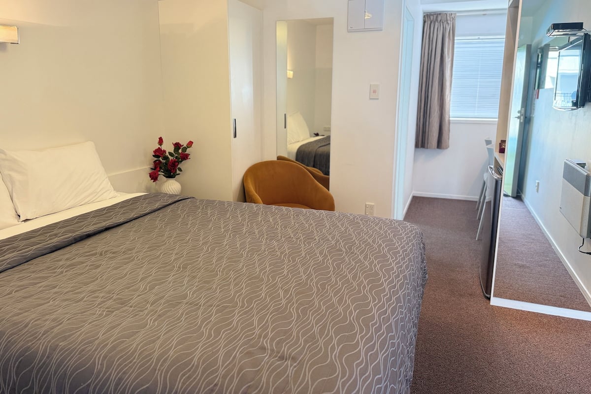A hotel room with a bed, a chair, a small table, and a window with curtains.