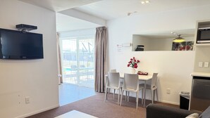 A modern living room with a flat-screen TV, a sofa, a dining table with chairs, and a kitchen area with a microwave. - Morrinsville Motel (Morrinsville)